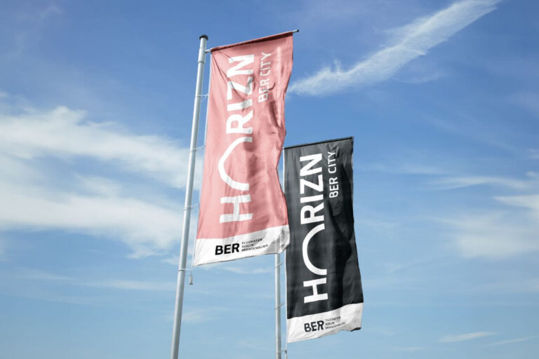 eine rosafarbene und eine schwarze Fahne mit dem Logo HORIZN BER CITY flattert im Wind