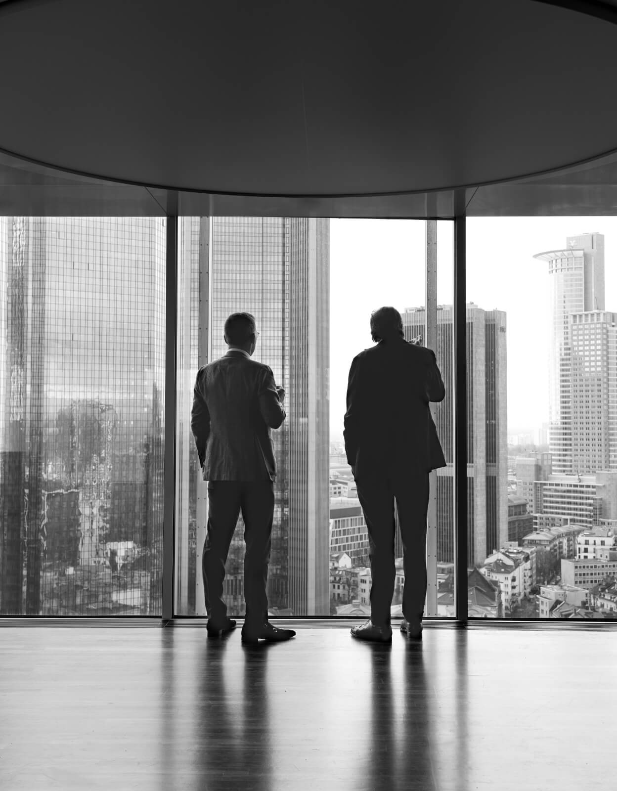 Zwei Männer vor einer großen Glasfront im Hintergrund Hochhäuser von Frankfurt in Schwarz weiß